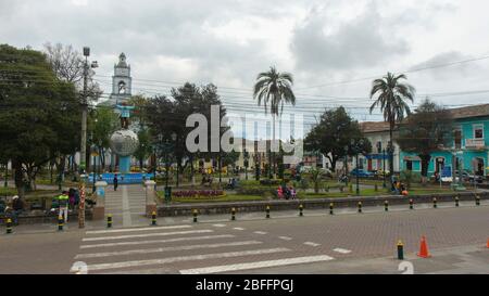 Cayambe, Pichincha / Ecuador - Februar 24 2020: Menschen sitzen im zentralen Park der Stadt mit der Matriz-Kirche im Hintergrund Stockfoto