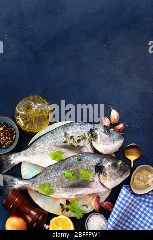 Vertikaler Schuss roher Fische mit den kochenden Zutaten auf dunkel Blauer Hintergrund Stockfoto