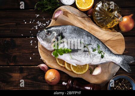 Draufsicht auf einen rohen Fisch auf Holzbrett mit Zutaten Stockfoto