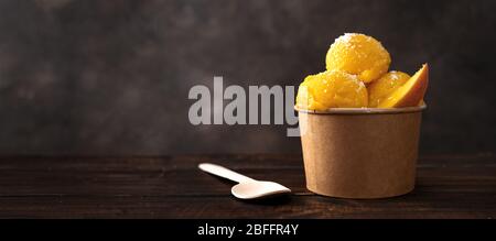 Mango-Sorbet in einem handwerklichen Papierbecher mit Holzlöffel Stockfoto
