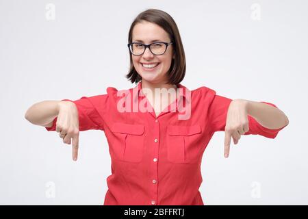 Junge lächelnde Frau zeigt mit Zeigefinger isoliert auf weiße Wand. Positive menschliche Emotion im Gesicht. Stockfoto