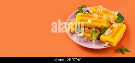 Vegane Mango-Sorbet-Eiszapfen auf trendigem, leuchtendem orangefarbenen Hintergrund Stockfoto