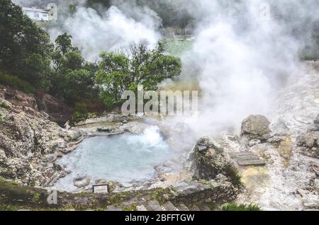Furnas, Sao Miguel, Azoren, Portugal - 13. Januar 2020: Vulkanische heiße Quellen in Portugiesisch Furnas. Geothermische Schwefelquelle. Dampf um die Wasserbecken. Stockfoto