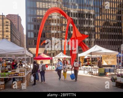 Ein samstags Bauernmarkt wird Flamingo gegenübergestellt, ein stabiler, von dem amerikanischen Künstler Alexander Calder auf dem Federal Plaza vor dem Kluczynski Federal Building in Chicago, Illinois, Stockfoto