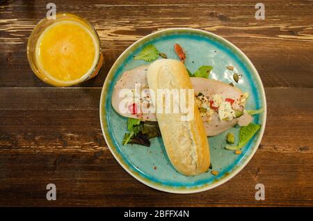 Ein kleines französisches Baguette, auch bekannt als Schlagstock (Stock), serviert mit einer Scheibe Schinken als Sandwich zusammen mit Orangensaft zum Frühstück. Stockfoto