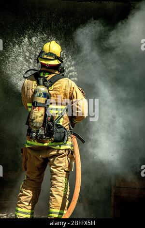 Ein Feuerwehrmann trägt Atemgeräte und sprüht Wasser in einer Demonstration eines Baubrands der Feuerwehr Costa Mesa, CA. Stockfoto