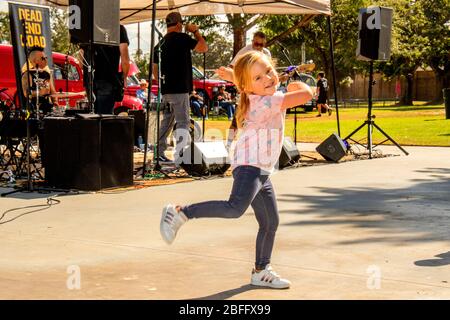 Ein dreijähriges Mädchen tanzt begeistert zu einer Rockband auf einer Freiluftmesse in einem Park in Costa Mesa, CA. Stockfoto