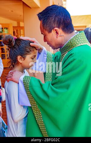 Ein geeinter vietnamesischer amerikanischer Priester segnet einen jungen Gemeindepfarrer nach der Messe in einer katholischen Kirche in Südkalifornien. Stockfoto