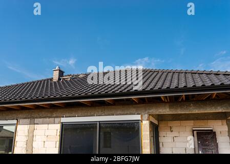 Das Dach eines Einfamilienhauses mit einer neuen Keramikfliesen in anthrazit gegen den blauen Himmel bedeckt, sichtbare Dachstühle. Stockfoto