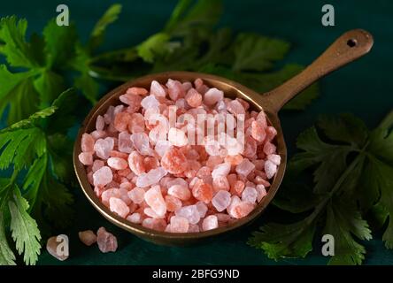 Rosa Himalaya-Salz mit frischem Cilantro in einem antiken Behälter auf einer grünen Oberfläche Stockfoto