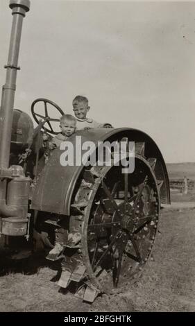 Schwarz-Weiß-Foto von zwei Brüdern auf einem Traktor. Fotografiert in den 1930er Jahren in Montana. Stockfoto