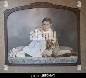 1930er-Porträt eines sitzenden Bruders und einer Schwester in einem Atelier. Der Junge trägt einen argyle-Pullover und das Mädchen ist in einem Kleid. Stockfoto