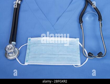 Draufsicht flache Lage einer chirurgischen Maske auf blauen Scrub oben mit schwarzen Doppel-Lauf Stethoskop um den Hals geloopt. Stockfoto