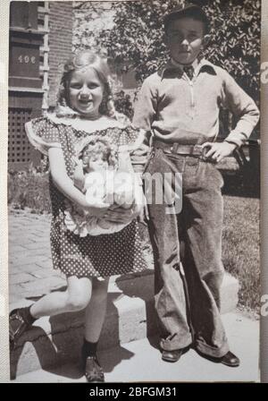 Vintage schwarz-weiß Foto von einem Bruder und Schwester mit dem Mädchen, das Puppe hält und ein Kleid mit einem Tupfen trägt. Stockfoto