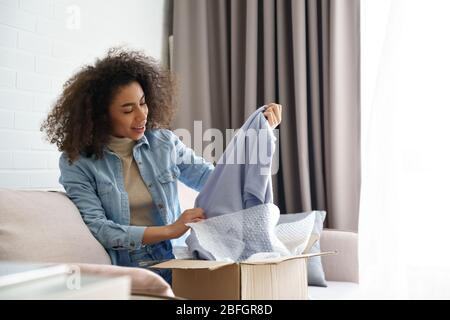 Erstaunt african junge Mädchen Kunde Auspacken Mode Lieferung box zu Hause. Stockfoto