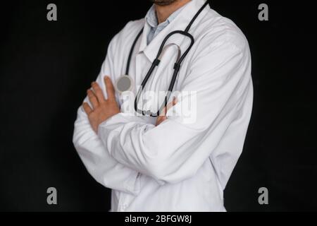 Männlicher Doktor auf schwarzem Hintergrund mit einem Stethoskop in den Händen Nahaufnahme. Stockfoto