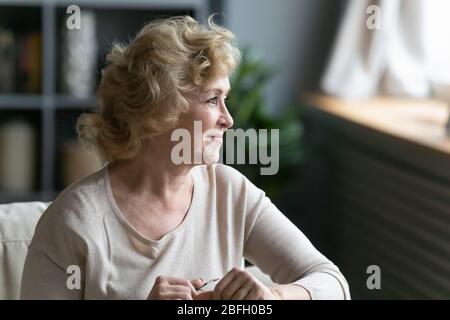 Lächelnde ältere Frau, die auf dem Sofa sitzt und aus dem Fenster schaut Stockfoto