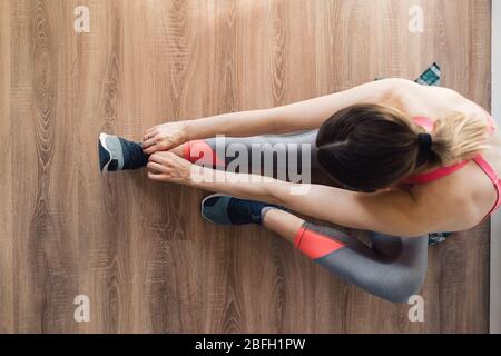 Junge sportliche Frau, die ihre Sportschuhe festbindet, während sie im Wohnzimmer auf dem Boden sitzt Stockfoto