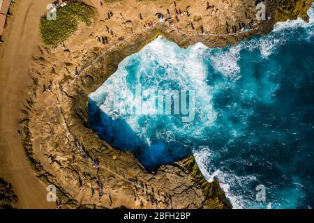 Luftaufnahme von Menschen, die sich versammeln, um riesige Wellen des Ozeans gegen eine felsige Inselküste zu brechen (Devil's Tears, Nusa Lembongan, Indonesien) Stockfoto