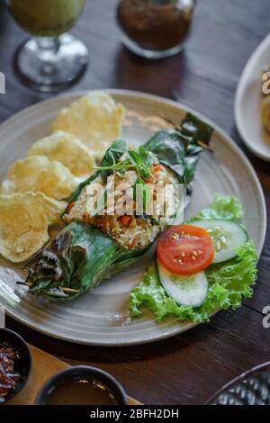 Gegrillter Thunfisch-Reis auf einem Keramikplatte serviert. Einige Begleiter wurden hinzugefügt: Melinjo-Chips (Gnetum gnemon), Basilikumblätter, Tomaten, Gurken und Salat. Stockfoto