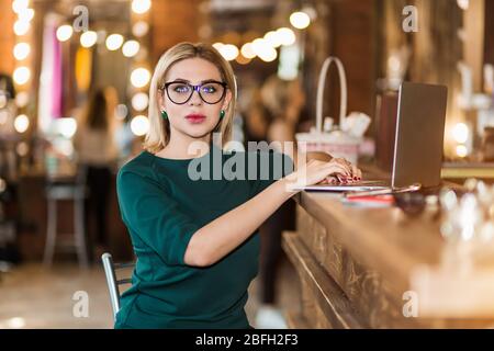 Portrait of Beauty Salon empfangsdame am Arbeitsplatz. Ernsthafte charmante Business Frau im grünen Pullover sitzen auf Stuhl mit den Händen auf die Tastatur, Schreiben, Stockfoto