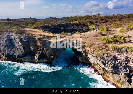 Luftaufnahme der Meereswellen, die durch einen Felsbogen in eine runde, isolierte Bucht stürzen (Broken Beach, Nusa Penida, Indonesien) Stockfoto