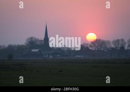 Sonnenuntergang über der holländischen Landschaft. Kirchturm ist gegen einen lila Himmel silhouetted. Stockfoto