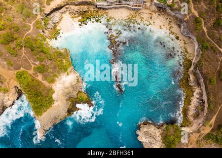 Draufsicht auf Wellen, die in einer kleinen felsigen Bucht brechen (Blaue Lagune, Nusa Ceningan, Indonesien) Stockfoto