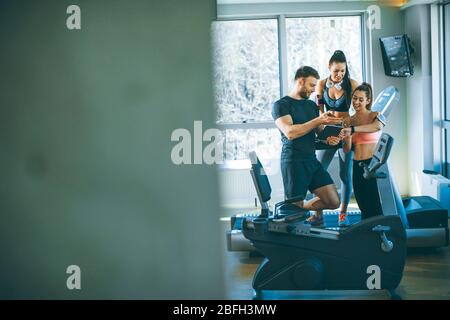 Personal Trainer, die sich das digitale Tablet anschaut und jungen Frauen im Fitnessstudio den Fortschritt erklärt Stockfoto