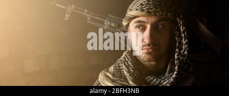 Arabischer Soldat im Kopfschmuck aus dem Nationalkeffiyeh mit einer Waffe in den Händen. Muslimischer Mann mit einer Pistole auf schwarzem Hintergrund. Stockfoto