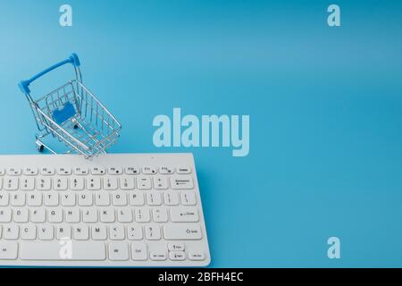 Leerer Lebensmittelwagen mit Tastatur auf blauem Hintergrund. Online Shopping, Internet Shopping Konzept Stockfoto