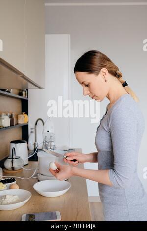 Schöne Frau brechen Hühnereier in einem Teller in der Küche. Teig kochen. Stockfoto