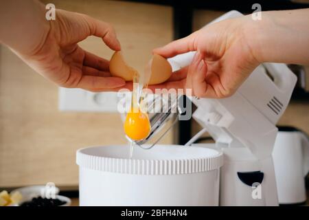 Nahaufnahme Hände brechen Hühnereier in einer Rührschüssel in der Küche. Teig kochen. Stockfoto