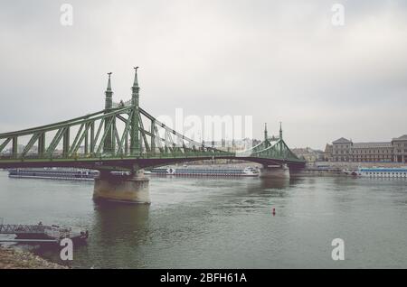 Budapest, Ungarn - 6. Nov 2019: Freiheitsbrücke über die Donau an einem nebligen, regnerischen Herbsttag. Kreuzfahrtschiff und historisches Zentrum im Hintergrund. Vertikales Foto. Ungarische Hauptstadt Stadtbild. Stockfoto
