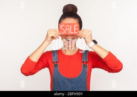 Mega-Rabatte! Porträt von glücklich erstaunt Mädchen mit Haar Bun in Denim Overalls, die Augen mit Verkauf Wort und schreiend in Erstaunen, von niedrig schockiert Stockfoto