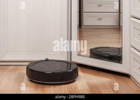 Reflection von schwarzen Roboter-Staubsauger läuft auf Laminatboden vor dem Spiegel im Schlafzimmer. Moderne intelligente Gerät für die Reinigung Haus. Stockfoto