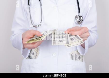 Beschnittenes Nahaufnahme von Frau Doktor, die die Anzahl der Banknoten in ihren Taschen auf grauem Hintergrund isoliert überprüft Stockfoto