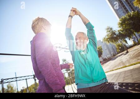 Morgenübungen. Glücklich reifen Familie Paar in Sportbekleidung Aufwärmen zusammen im Outdoor-Fitnessstudio am Morgen, sie tun Dehnungsübungen Stockfoto