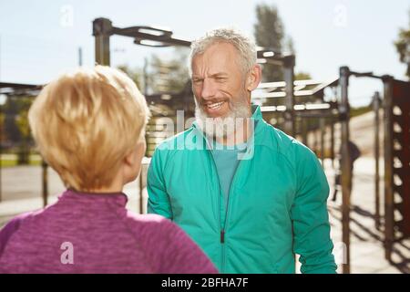 Aktiver Morgen. Happy Senior Familie Paar ist Sport im Freien. Reife bärtige Mann in Sport tragen Gespräch mit seiner Frau während der Arbeit zusammen Stockfoto