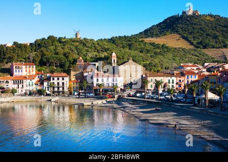 Collioure, Frankreich - Februar 24, 2020: Strandhotels in Collioure Dorf mit einer Windmühle auf der Spitze des Hügels, Roussillon, Vermilion Küste, Pyrenäen Stockfoto