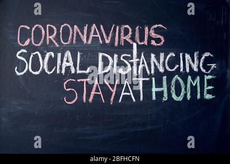 Aufschrift soziale Distanzierung bleiben zu Hause. Warnung vor Ausbruch. Weiße Kreide auf Tafel im Zusammenhang mit der Epidemie von Coronavirus weltweit geschrieben. Stockfoto