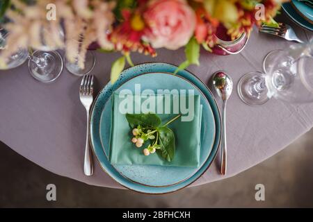 Keramikplatten und anderes Besteck sind auf einem Holztisch mit weichen Tischdecken für ein luxuriöses Mittagessen angeordnet. Stockfoto