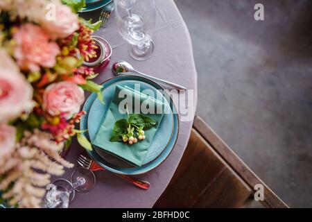 Keramikplatten und anderes Besteck sind auf einem Holztisch mit weichen Tischdecken für ein luxuriöses Mittagessen angeordnet. Stockfoto