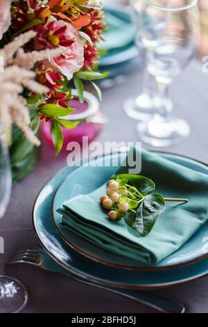 Keramikplatten und anderes Besteck sind auf einem Holztisch mit weichen Tischdecken für ein luxuriöses Mittagessen angeordnet. Stockfoto