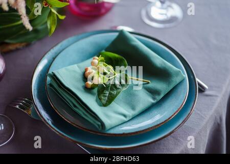 Keramikplatten und anderes Besteck sind auf einem Holztisch mit weichen Tischdecken für ein luxuriöses Mittagessen angeordnet. Stockfoto