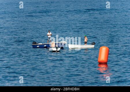 Drei Männer, jeder in seinem eigenen kleinen Boot, unterhalten sich mitten im Meer in der Nähe einer großen orangefarbenen Boje. Ligurien, Italien, Europa Stockfoto