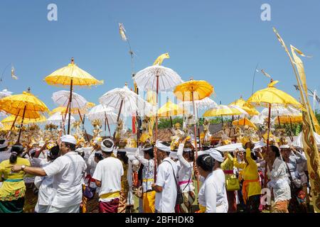 Bali, Indonesien - März 2019: Die Balinesen versammeln sich und bringen hölzerne Regenschirme und Banner mit, während sie das Feld für die Einäscherung umrunden Stockfoto