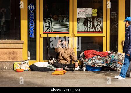 Ein Obdachloser mit seinem Hund bittet an einem Wintersonntag vor einer Bank in der Via Rizzoli, in der Innenstadt von Bologna, um Almosen. Emilia-Romagna, Italien, Europa Stockfoto