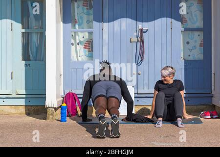 Bournemouth, Dorset, Großbritannien. April 2020. UK Wetter: Schöner warmer sonniger Tag, da die Temperaturen an den Stränden von Bournemouth an der Südküste steigen, während die Menschen ihre erlaubte Bewegung machen, die meisten halten sich an die Coronavirus Richtlinien. Junge Frau beobachtet Mann tun Liegestützübungen von Strandhütten. Quelle: Carolyn Jenkins/Alamy Live News Stockfoto