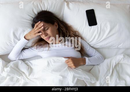 Unglückliche Frau, die Kopfschmerzen nach dem plötzlichen Erwachen durch Telefonat hat Stockfoto